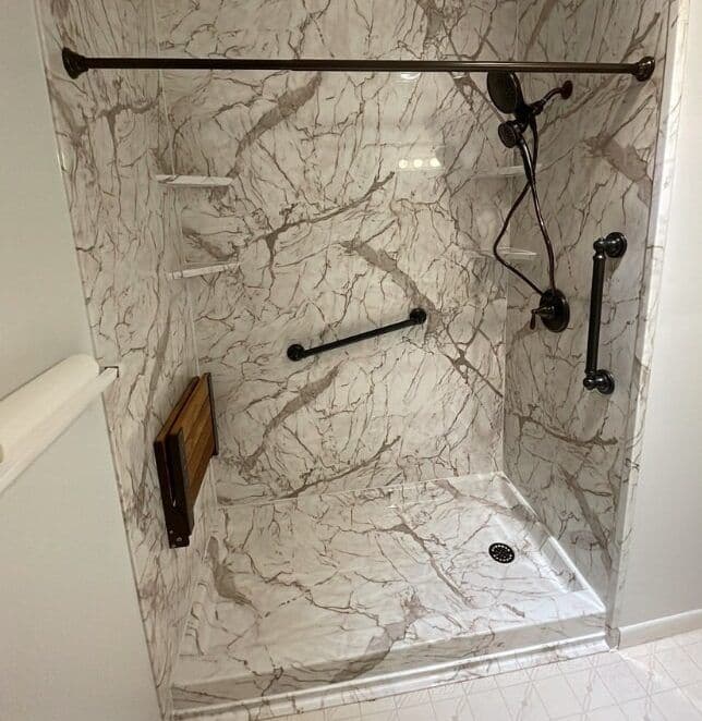 A walk-in shower with multiple grab bars, folding bench seat, corner shelves, black fixtures, and marbled walls.