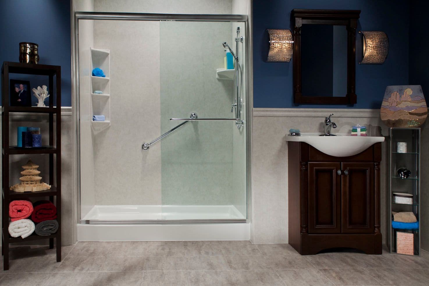 A dark blue bathroom with a walk-in acrylic shower with sliding glass doors and diagonal grab bar.